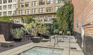 A rooftop pool area with lounge chairs, potted plants, and a building in the background.