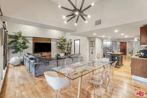 A spacious living area with a glass dining table, grey sofa, and a modern ceiling light fixture.