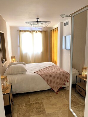 A bedroom with a bed, curtains, a ceiling fan, a bedside table with a lamp, and a mirror. - Single-storey house in the Capucins district - near Paicherou swimming pool and Cité (Carcassonne)