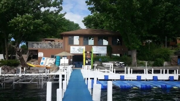 A dock leading to a building with a signboard, a blue pathway, and a water body.