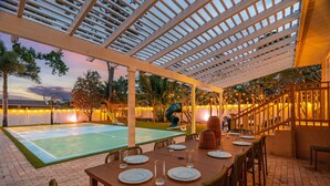 Un espacio de comedor al aire libre con cancha de baloncesto, asientos techados y vista al atardecer.