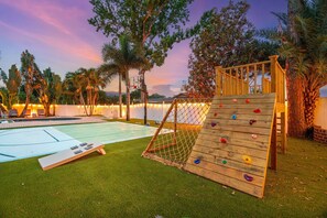 A rock climbing wall, a pool, and a grassy area with trees.