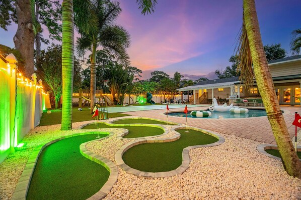 A pool area with a fountain, palm trees, and a building with a porch.