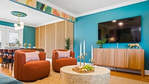 Una sala de estar con una pared azul verdoso, un televisor de pantalla plana, un mueble de madera y dos sillones naranja.