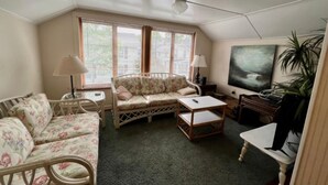 Um quarto aconchegante com um sofá, uma mesinha, uma cadeira e um quadro na parede.
