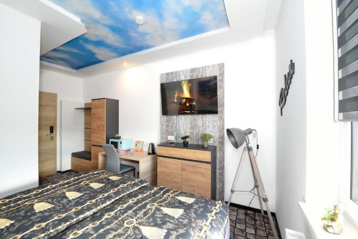 A modern bedroom with a bed, desk, wardrobe, and a TV mounted on the wall.