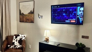 Un salon avec un fauteuil en cuir marron, une petite table avec une lampe, un téléviseur fixé au mur et un panneau indiquant qu'il est interdit de fumer.