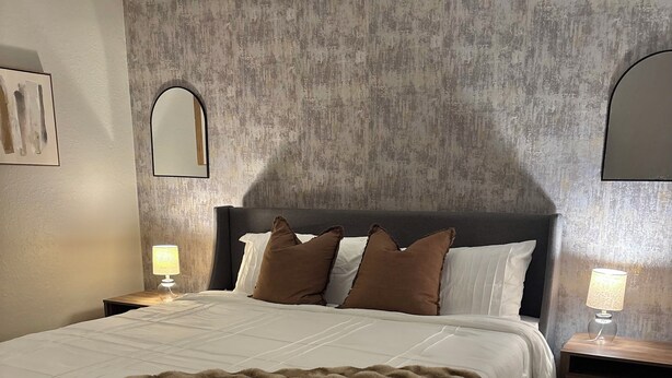 Une chambre d’hôtel avec un grand lit, deux lampes de chevet, un tapis à motifs et un mur à texture.
