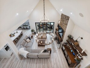 Un loft espacioso con techo alto, zona de estar central con candelabro, chimenea y cocina equipada con electrodomésticos modernos.