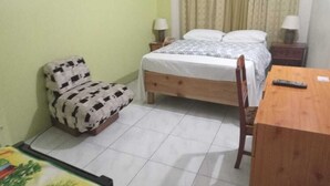 Une petite pièce propre, avec un lit, une chaise, une table en bois et une table de chevet avec une lampe.