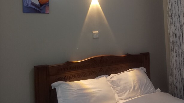 A bed with white linens, a wooden headboard, and a wall-mounted light fixture. - Tranquil 1-bedroom house perfect for a relaxing Nairobi getaway (Nairobi)