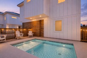 Ein Schwimmbecken mit Holzdeck und Liegestühlen, umgeben von einem weißen Gebäude mit Holzzaun.
