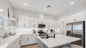 Una cucina moderna con mobili bianchi, elettrodomestici in acciaio inossidabile e un'isola centrale con sgabelli.