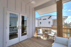 Eine überdachte Terrasse im Freien mit Holzboden, weißen Wänden und einer Glastür zu einem Raum mit einer Couch und einem Tisch.