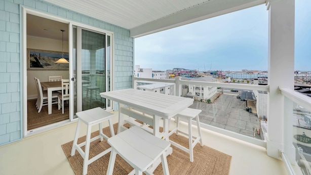 Een balkon met een tafel en stoelen, een glazen deur naar een eethoek binnen, en uitzicht op een stadsgezicht.