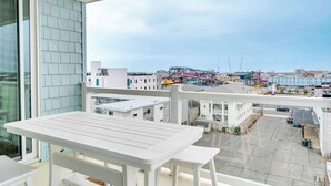 Een balkon met een witte tafel en stoelen, met uitzicht op een parkeerplaats en gebouwen met kranen.