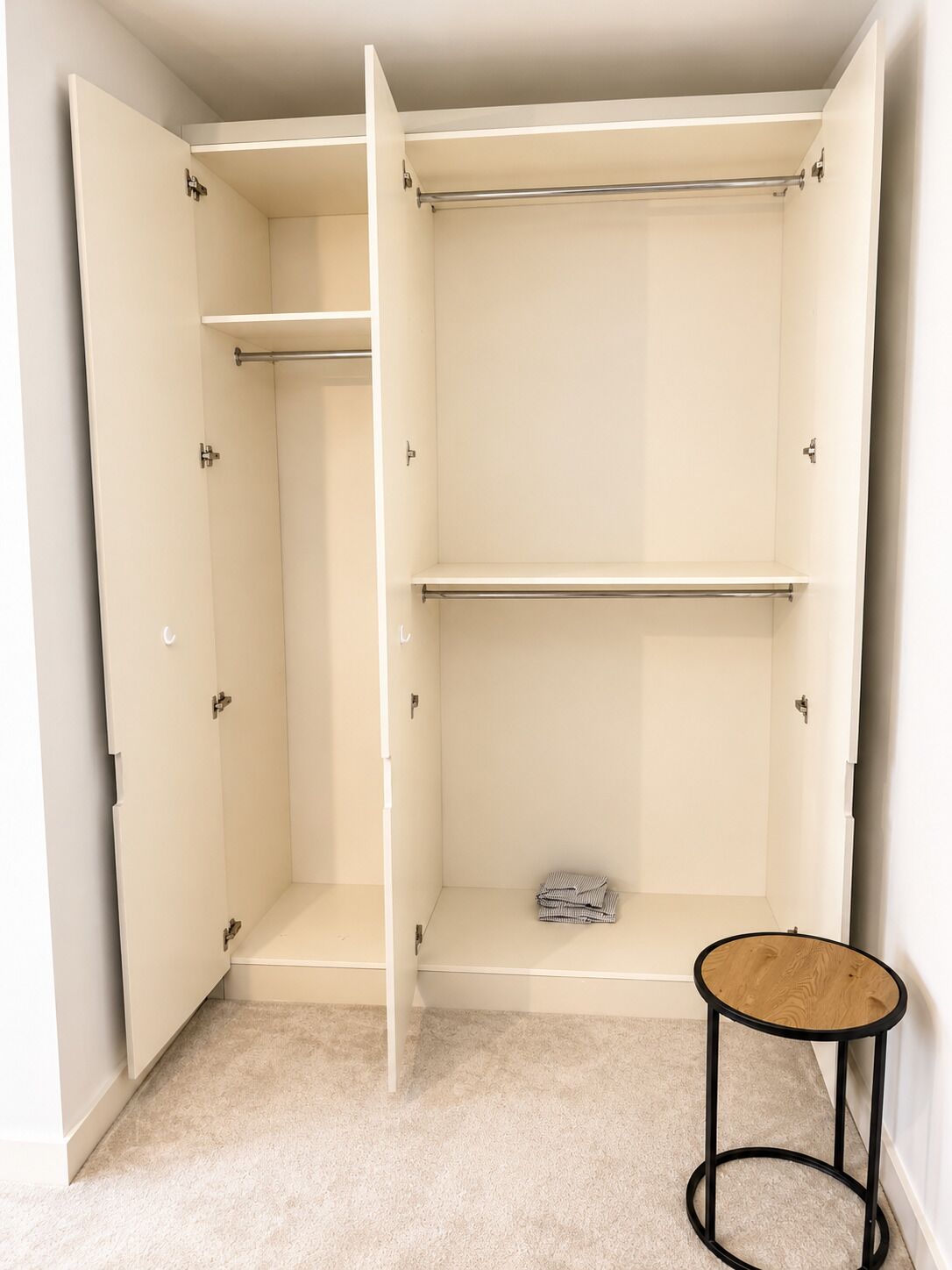 A walk-in closet with open doors, a hanging rod, and a small round table.