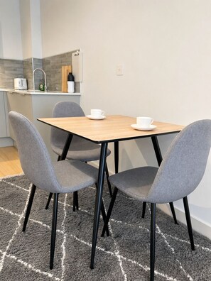 A modern kitchen with a dining area, including a table with four chairs, a rug, and a countertop with a toaster and a bottle. - Apartment in Birmingham JQ Area Free WiFi & Parking.  (Birmingham)