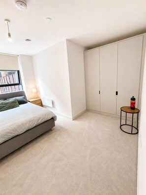 A bedroom with a bed, a nightstand, a lamp, a wardrobe, and a small table with a bottle. - Apartment in Birmingham JQ Area Free WiFi & Parking.  (Birmingham)