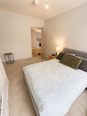 A bedroom with a bed, bedside table, lamp, and a view into the kitchen. - Apartment in Birmingham JQ Area Free WiFi & Parking.  (Birmingham)