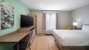 Ein Hotelzimmer mit Bett, Schreibtisch, Stuhl, Fernseher und einem fenster mit Vorhängen.