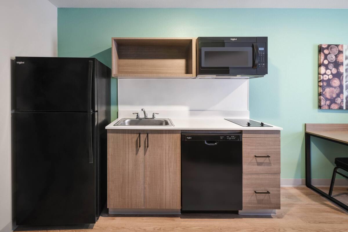 Una cocina compacta con un refrigerador negro, un microondas, un lavavajillas y armarios de madera.