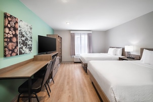 Habitación de hotel con escritorio de madera, televisor de pantalla plana, dos camas, ventana con cortinas y una obra de arte en la pared.