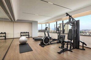A modern gym with exercise equipment, a large mirror, and a view of the city through large windows.