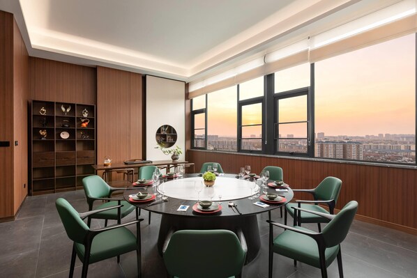 A modern conference room with a round table, green chairs, and a city view through large windows.