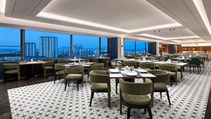 Ein modernes Restaurant mit Tischen, Stühlen, großen Fenstern und Blick auf die Stadt.