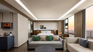 Ein modernes Hotelzimmer mit einem Bett, zwei Sofas, einem runden Tisch und Blick auf die Stadt.