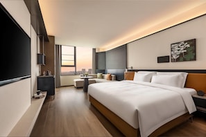Ett modernt hotellrum med en stor säng, ett skrivbord, en TV och utsikt över staden.