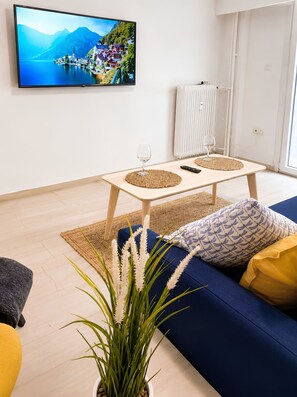 A living room with a television mounted on the wall, a sofa, a coffee table, and a potted plant. - Quiet Marina Zea, 3-Min Walk & Self Check-in (Piraeus)