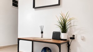 Een minimalistisch ingerichte kamer met een houten tafel, een blauwe decoratieve bal, een witte plant, een wandlamp en een witte robotstofzuiger.