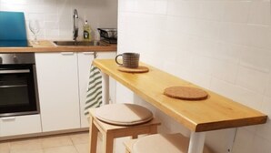 Een keuken met een houten tafel, twee krukken, een spoelbak en een fornuis.
