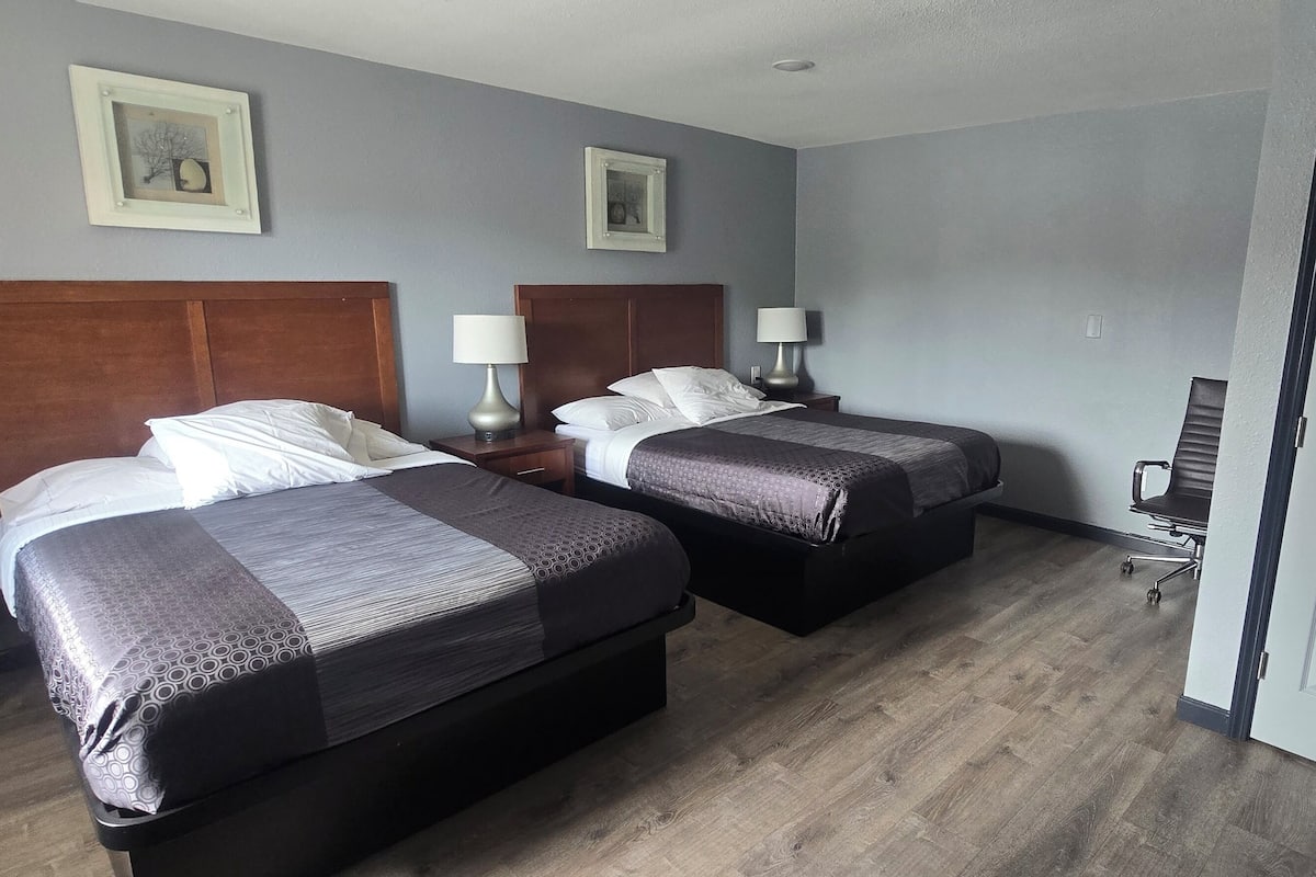 Habitación de hotel con dos camas, cabeceros de madera, mesitas de noche con lámparas y una puerta.