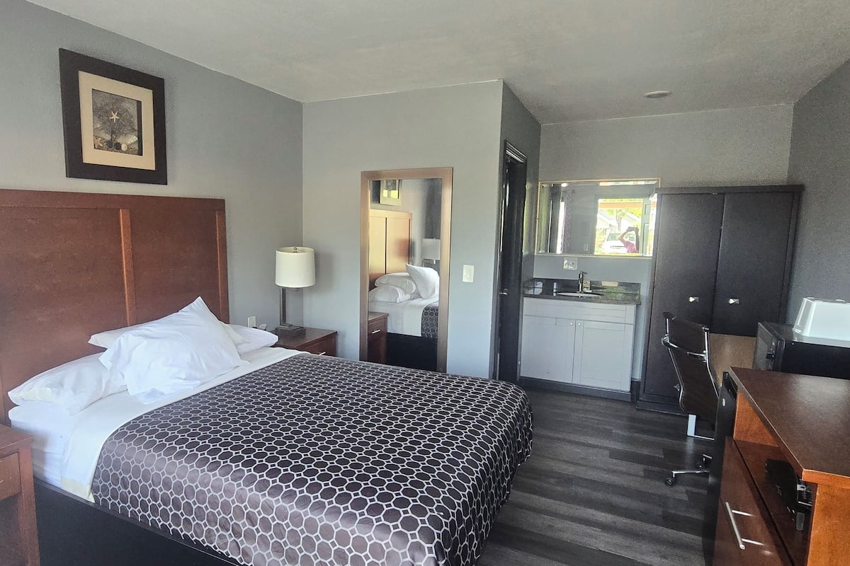 Una habitación de hotel con cama, lámparas de noche, escritorio, espejo, armario y kitchenette.
