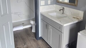 A bathroom with a marble wall, a white sink, a gold-framed mirror, and a wooden floor.