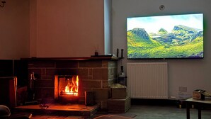 A living room with a fireplace, a mounted television, and a radiator. - Woodview (Isle of Barra)