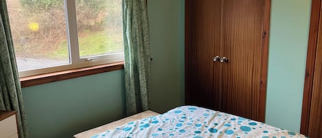 Ein Schlafzimmer mit Bett, einem Fenster mit Vorhängen, einem Holzschrank und einer Kommode.
