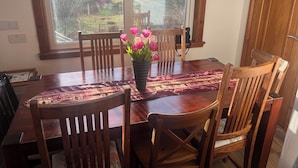 A dining table with chairs, a vase with flowers, and a view of a garden through a window. - Woodview (Isle of Barra)