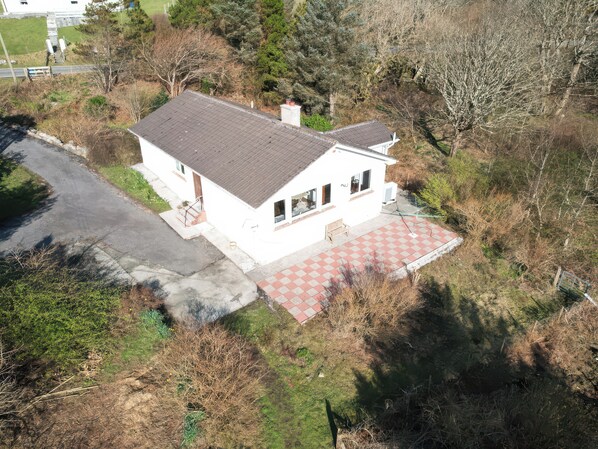 A single-story house with a red and white checkered patio, surrounded by trees and a grassy area.