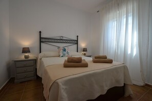 Ein Schlafzimmer mit einem Bett, zwei Nachttischen, einem Fenster mit Vorhängen und einem gefliesten Boden.