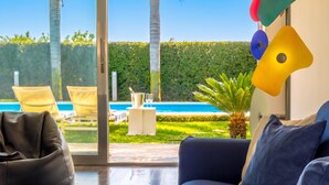 Ein modernes Wohnzimmer mit einer Couch, einem Glastisch und Blick auf einen Swimmingpool und Grünflächen.