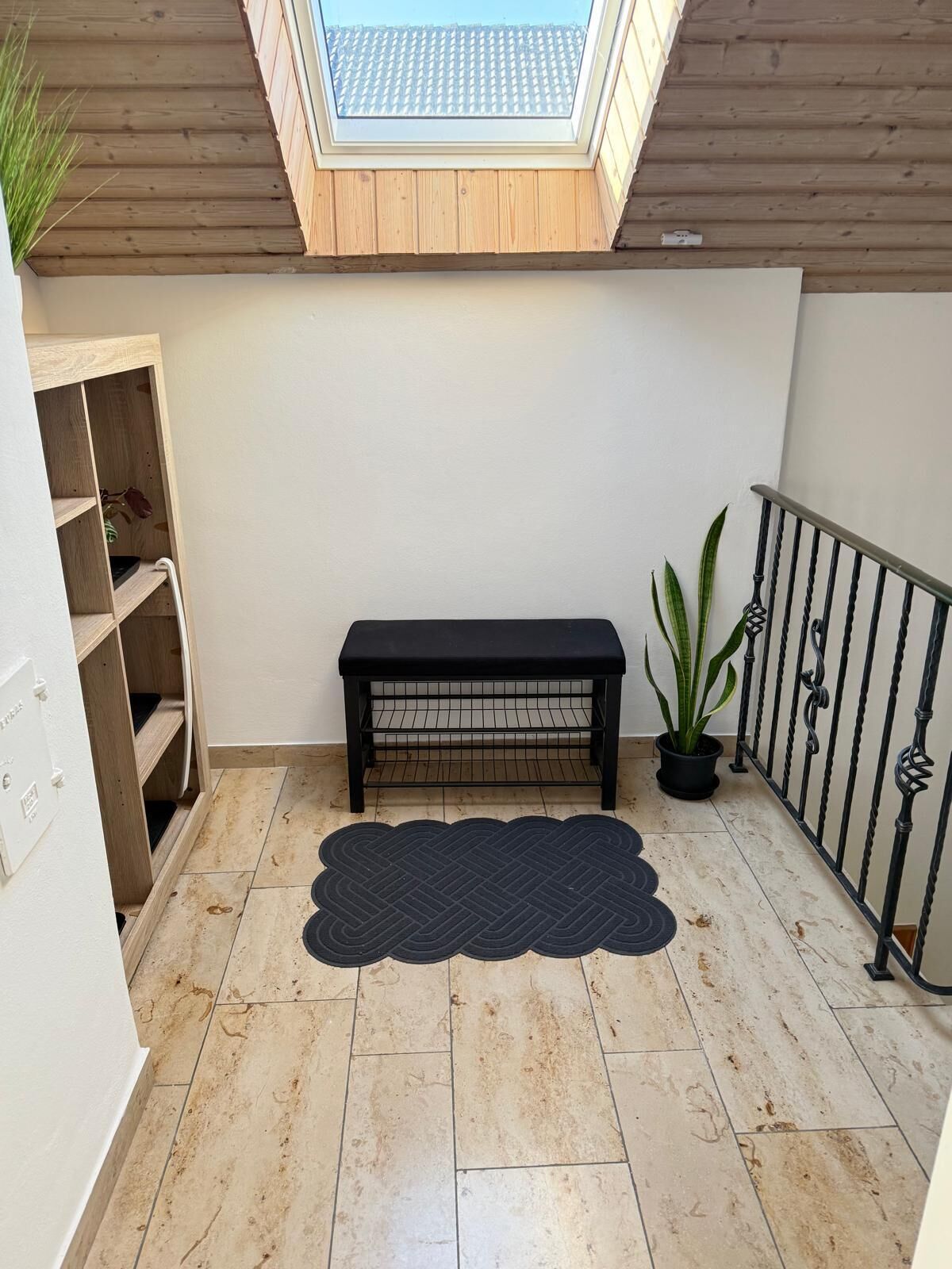 A room with a skylight, a black bench, a potted plant, and a tiled floor.
