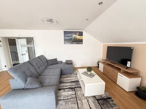 A modern living room with a sectional sofa, a flat-screen TV, a white coffee table, and a wooden TV stand.