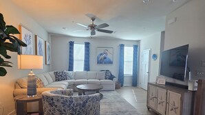 A living room with a sofa, coffee table, TV, and a ceiling fan. - Coastal Luxury Townhome in West Ocean City, 4 Bedrooms , Near Beach, Assateague (Berlin)