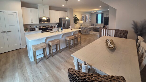 A modern kitchen with white cabinets, a central island with bar stools, a dining area with a large table, and a living room with a sofa and a TV. - Coastal Luxury Townhome in West Ocean City, 4 Bedrooms , Near Beach, Assateague (Berlin)