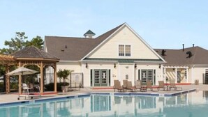 A swimming pool with lounge chairs and a gazebo, surrounded by a building with a gabled roof and windows. - Coastal Luxury Townhome in West Ocean City, 4 Bedrooms , Near Beach, Assateague (Berlin)