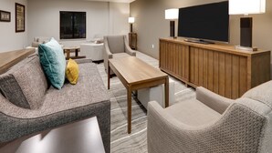 A modern living room with a sofa, armchairs, a wooden coffee table, a TV, and a lamp. - King Studio w/ Kitchen | Pool + Daily Breakfast (Oklahoma City)